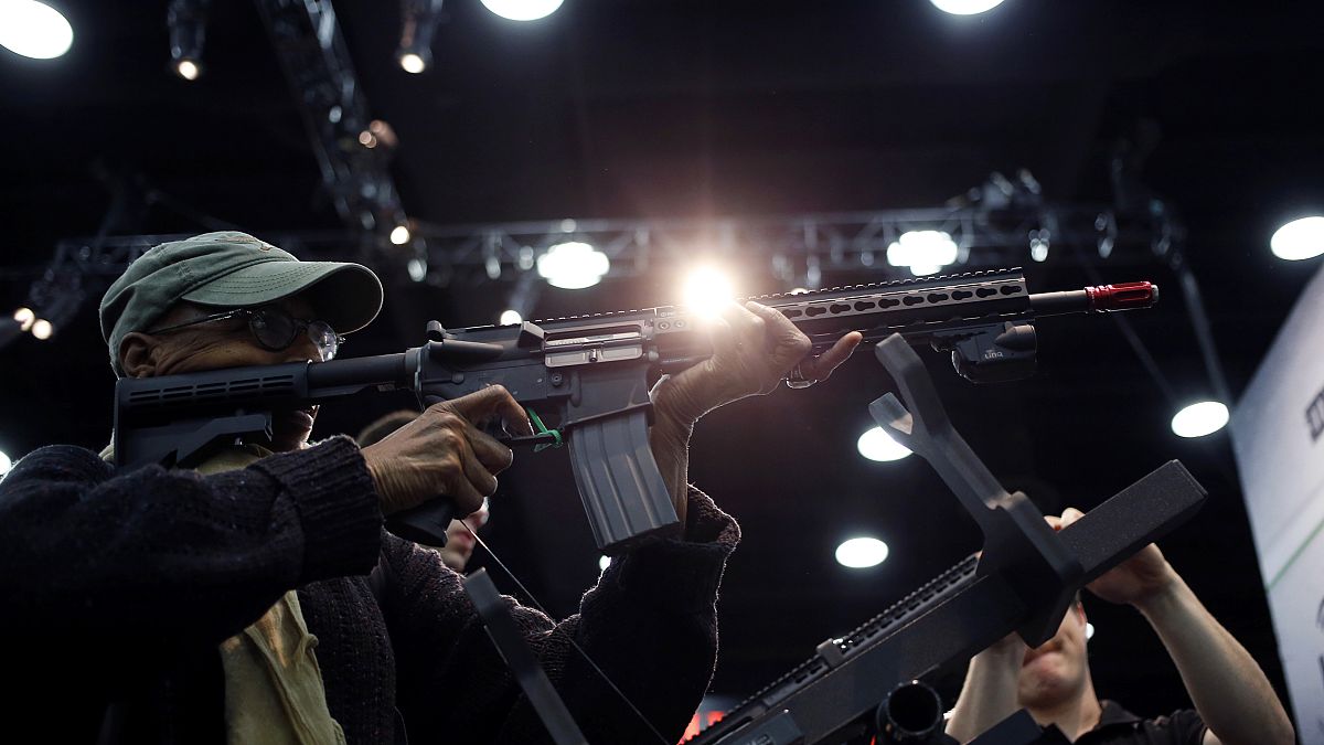 Image: An attendee holds an AR-15 style gun on the exhibit floor at the Nat