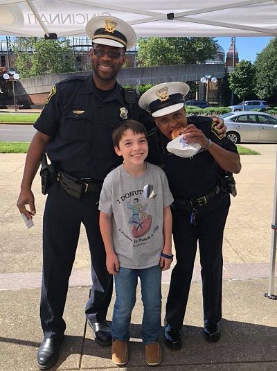 Though he used his allowance to buy the first four doughnuts, Tyler now relies on donations to deliver dozens of doughnuts at a time. Here he is with police officers in Cincinnati, Ohio.