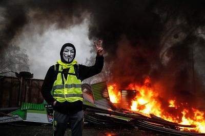 A masked "yellow vest" protester makes the victory sign near a burning barricade in Paris on Dec. 1.