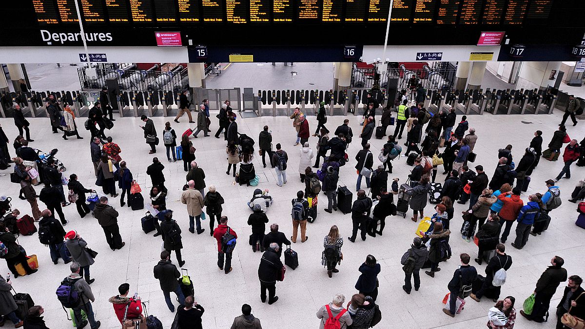 Image: Travelers wait near the departure boards at London's Waterloo train 