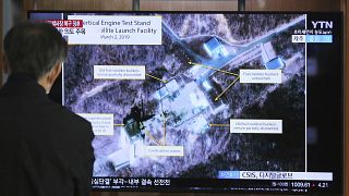Image: A man watches a TV screen showing an image of the Sohae Satellite La
