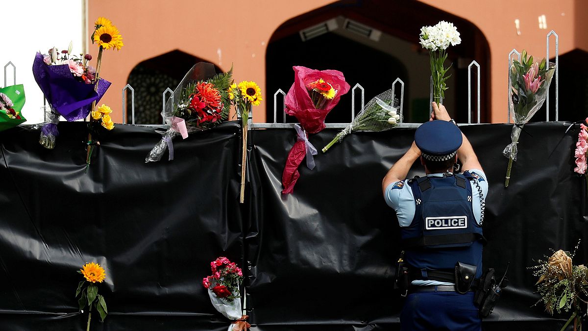 Image: A police officer places flowers at the entrance of Masjid Al Noor mo