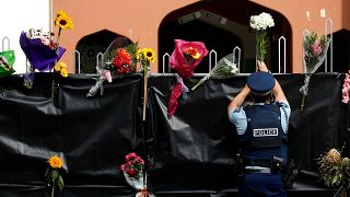 Image: A police officer places flowers at the entrance of Masjid Al Noor mo