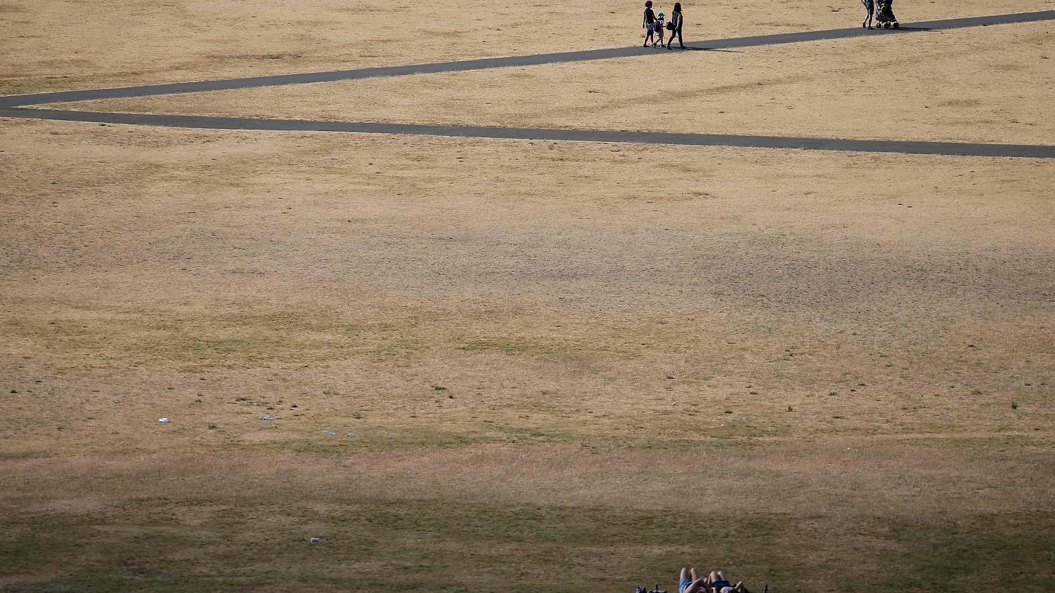 Image: Visitors to Greenwich Park walk on the footpaths in between the dry 