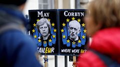 Image: Pedestrians walk past placards featuring Britain's Prime Minister Th