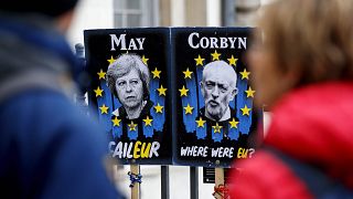 Image: Pedestrians walk past placards featuring Britain's Prime Minister Th