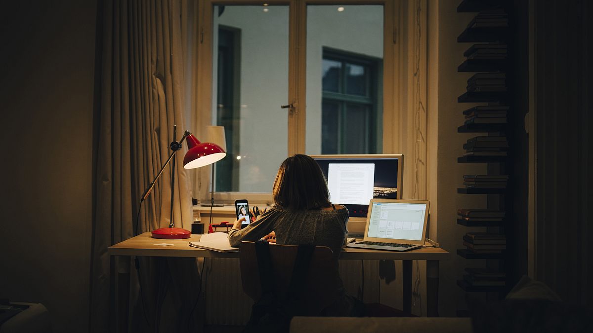 Girl using laptop and computer while sitting at illuminated desk