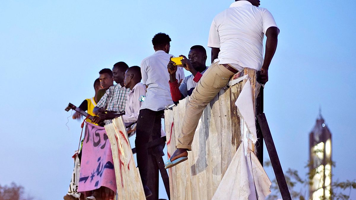 Image: Protesters sit on a torn billboard in Khartoum, Sudan
