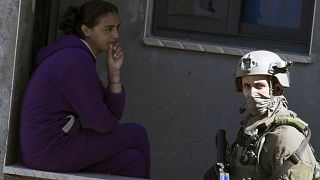 Image: An Israeli soldier walks past a Palestinian girl