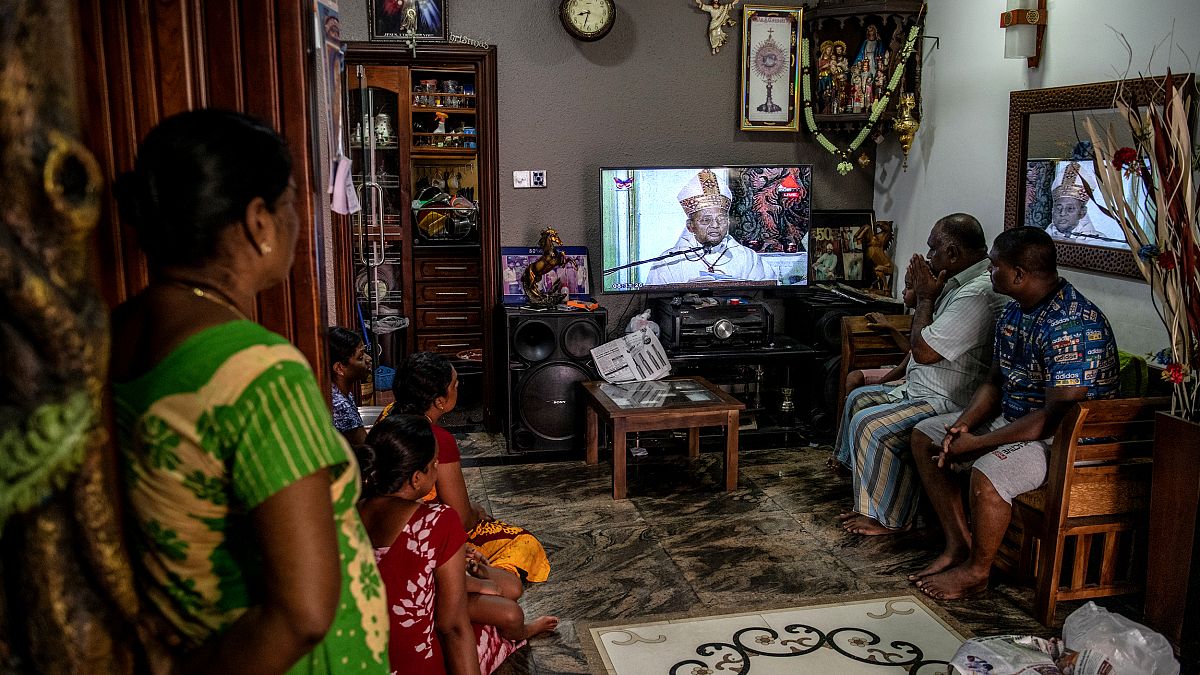 Image: A family watches a televised mass led by Cardinal Malcom Ranjith, a 
