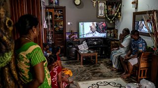 Image: A family watches a televised mass led by Cardinal Malcom Ranjith, a 