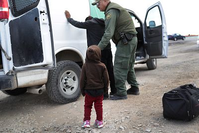 A child watches as a Border Patrol agent searches a Central American immigrant after they crossed the border from Mexico in El Paso, Texas on February 1, 2019.