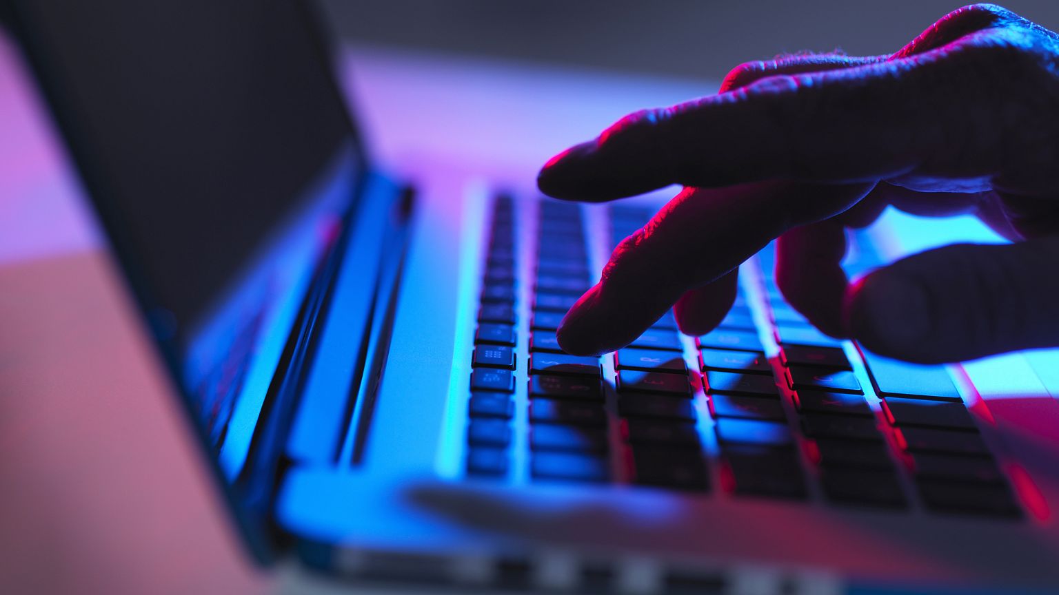 Silhouette of male hand typing on laptop keyboard at night