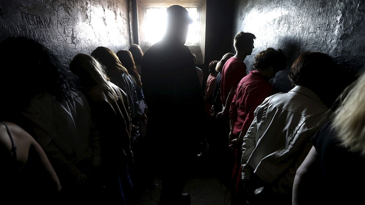 Image: People line up facing the walls as they attend a voluntary imprisonm