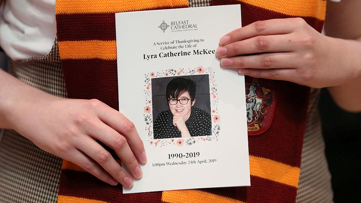 Image: A mourner wearing a Gryffindor scarf holds an order of service as sh