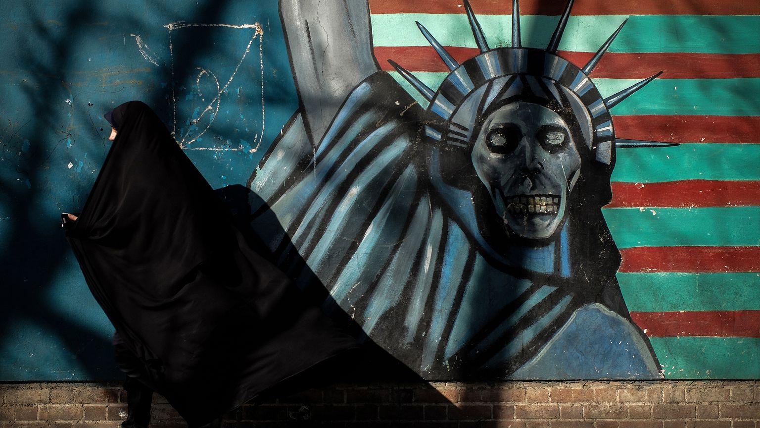 Image: An Iranian woman passes a mural painted on the wall of the former U.
