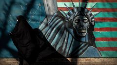 Image: An Iranian woman passes a mural painted on the wall of the former U.