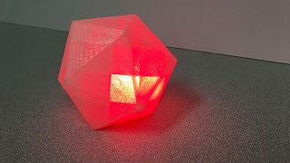 Image: A block-like geometric shape that emits a glowing red light when it 