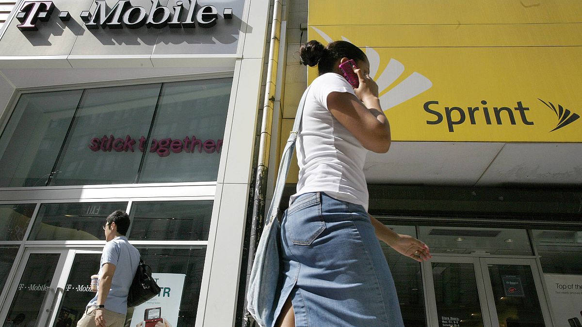 Image: A woman talking on her phone as she walks past T-mobile and Sprint w