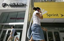 Image: A woman talking on her phone as she walks past T-mobile and Sprint w