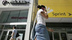 Image: A woman talking on her phone as she walks past T-mobile and Sprint w