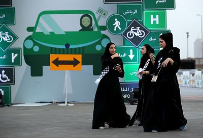 Young women wearing the traditional abaya walk past a sign as they help to organize an outdoor educational driving event for women on June 21, 2018 in Jeddah, Saudi Arabia