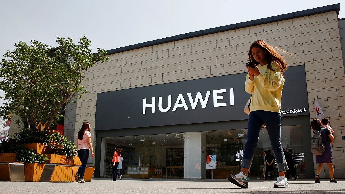 Image: FILE PHOTO: A woman looks at her phone as she walks past a Huawei sh