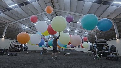Gökyüzünde 100 balon ve kamp sandalyesinde bir adam