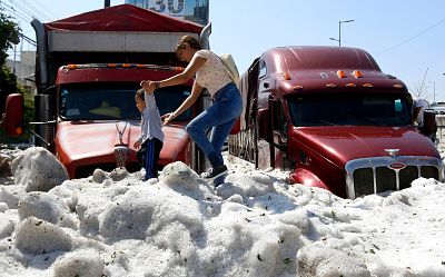 A woman and child walk on a pile of hail in Guadalajara, Mexico, on June 30, 2019.