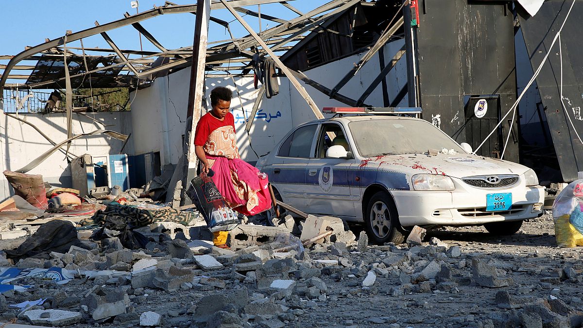 Image: A migrant picks up clothes from among rubble at a detention centre f