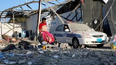 Image: A migrant picks up clothes from among rubble at a detention centre f