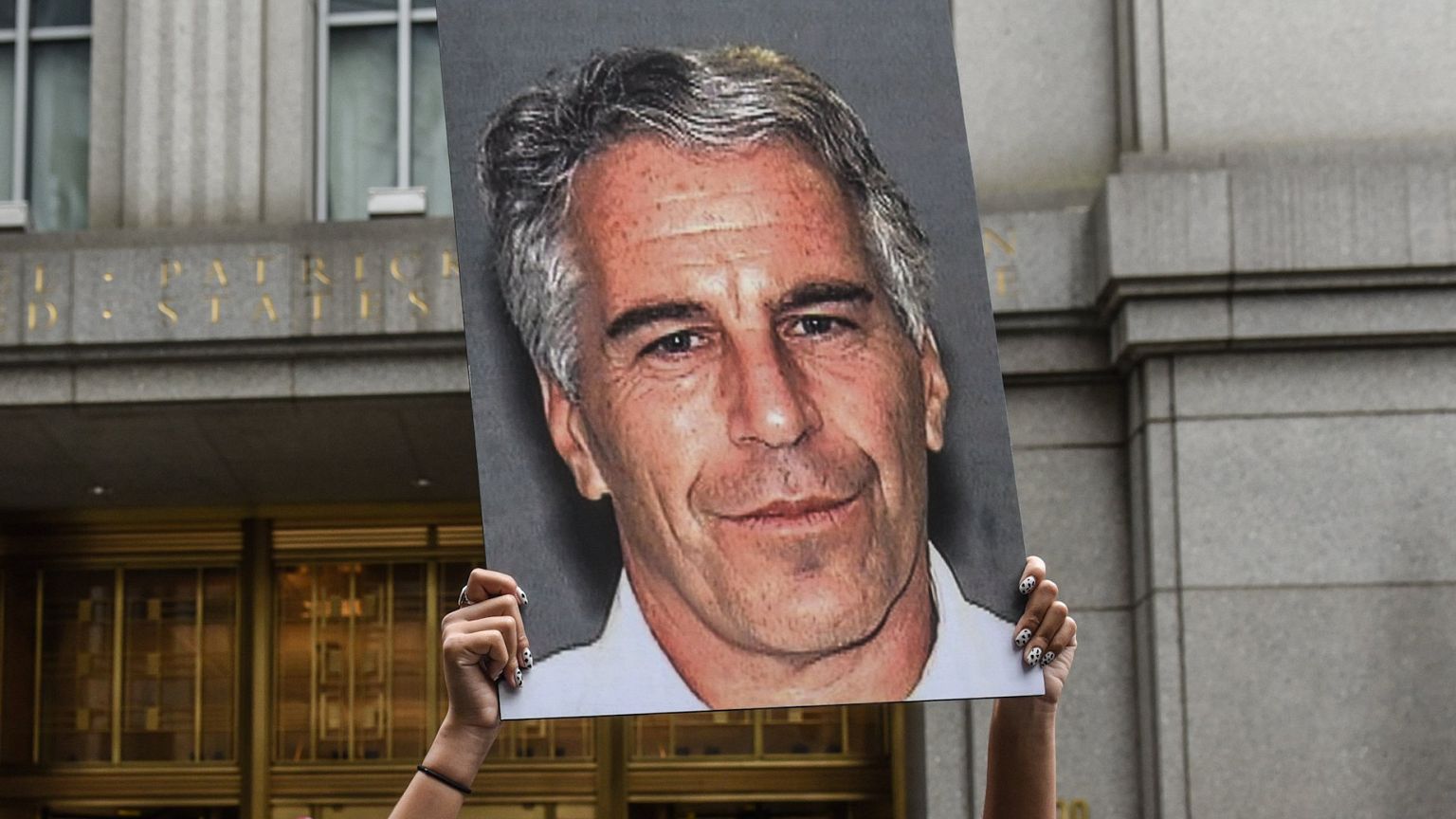 Image: A protester holds up a placard with a photo of Jeffrey Epstein in fr