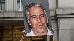 Image: A protester holds up a placard with a photo of Jeffrey Epstein in fr
