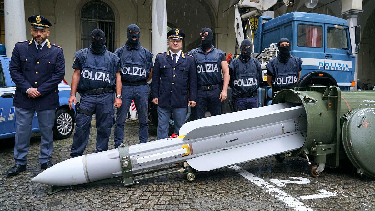 Image: Police stand with a missile seized at an airport hangar near Pavia a