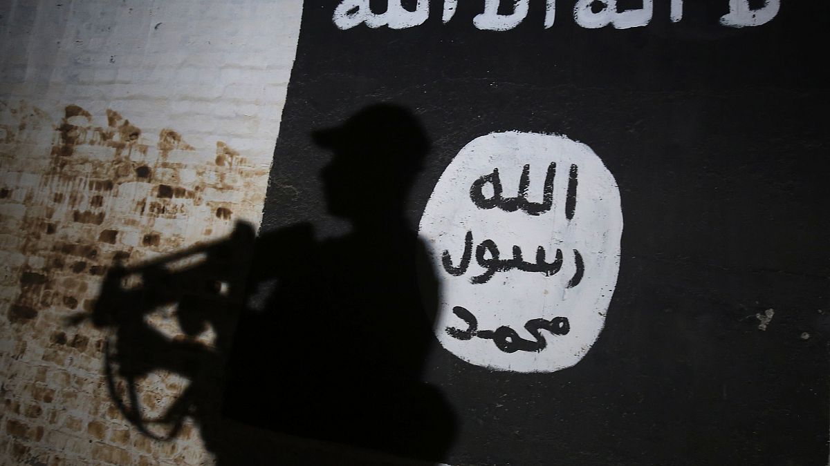 Image: An Iraqi forces member walks past a mural with the ISIS logo in the 