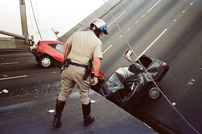 A California Highway Patrol Officer checks the damage to cars that fell when the upper deck of the Bay Bridge collapsed onto the lower deck after the Loma Prieta earthquake in San Francisco on Oct. 17, 1989.