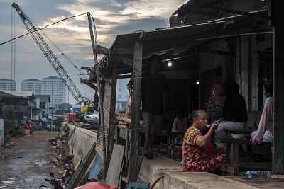 A woman eats her dinner in front of her home built on the old seawall from which the sea frequently spills over in Jakarta, Indonesia.