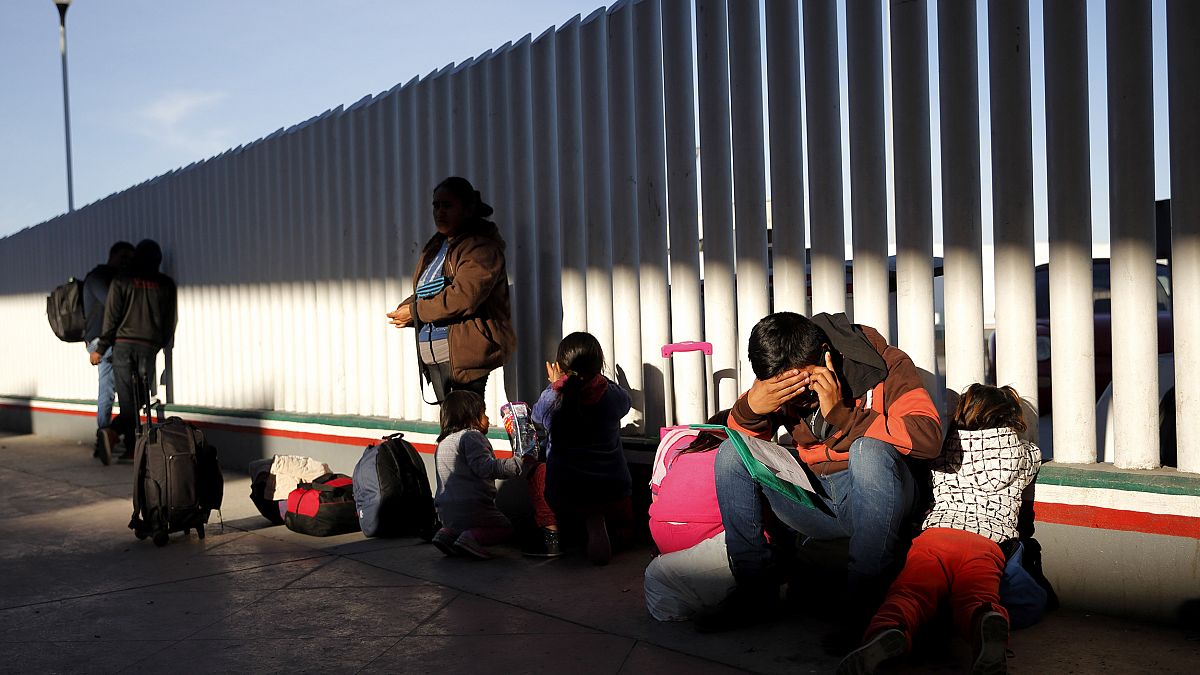 Image: A migrant sits with his children to apply for asylum to the United S