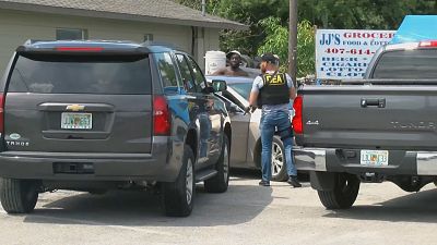 An armed DEA agent stands near vehicles during a raid.