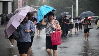 Image: Pedestrians shield themselves from wind and rain from Typhoon Lingli