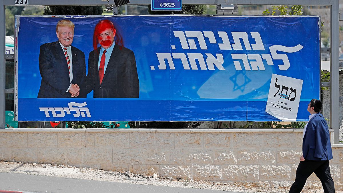Image: An Israeli man looks at a defaced election billboard for the Likud p