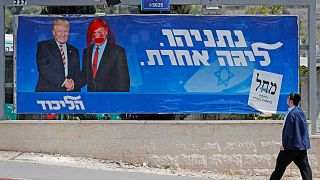 Image: An Israeli man looks at a defaced election billboard for the Likud p