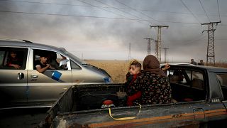 Image: A woman and her baby sit in the back of a truck as they flee Ras al-
