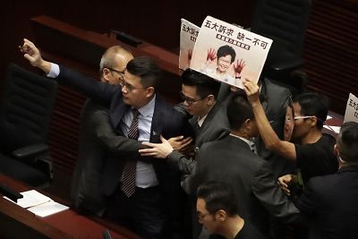 A pan-democratic legislator is restrained as he holds up a speaker playing what legislators said was audio of police tear-gassing demonstrators to protest while Hong Kong Chief Executive Carrie Lam attempts to speak at the Legislative Council in Hong Kong, Wednesday, Oct. 16, 2019.