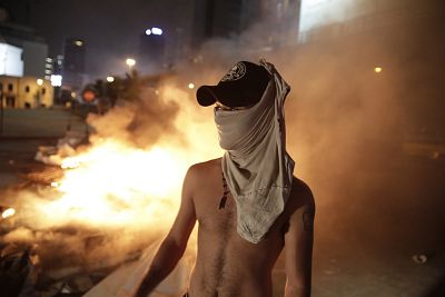 An anti-government protester stands by a fire of plastic barriers and trash to block a road during a demonstration in Beirut, Lebanon on Oct. 17, 2019.
