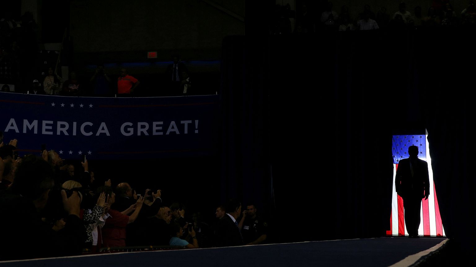 Image: President Donald Trump is silhouetted against a U.S. flag as he hold