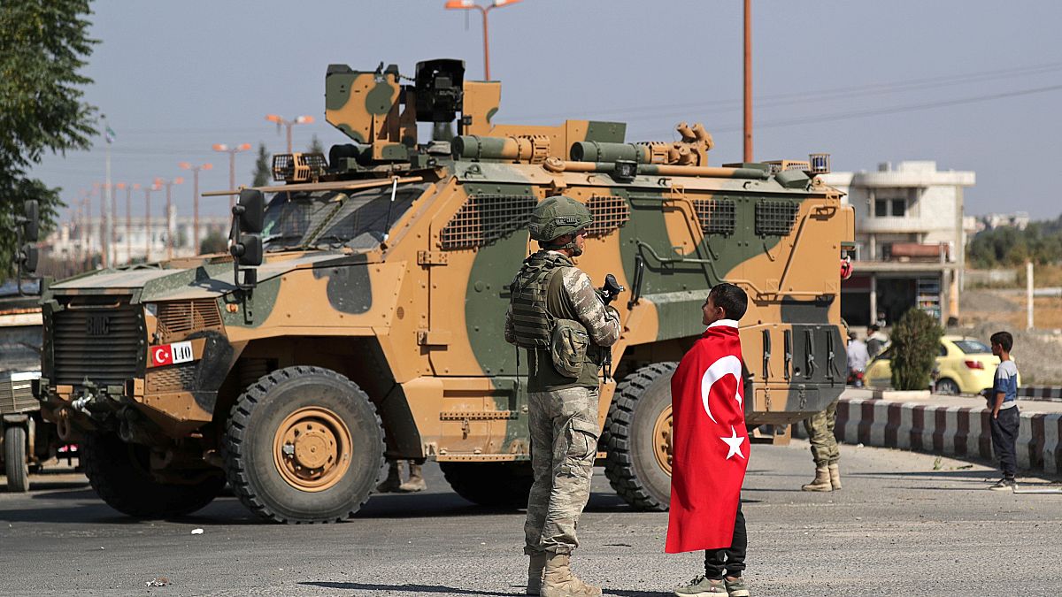 Boy wearing a Turkish flag stands next to a Turkish soldier in the town of 