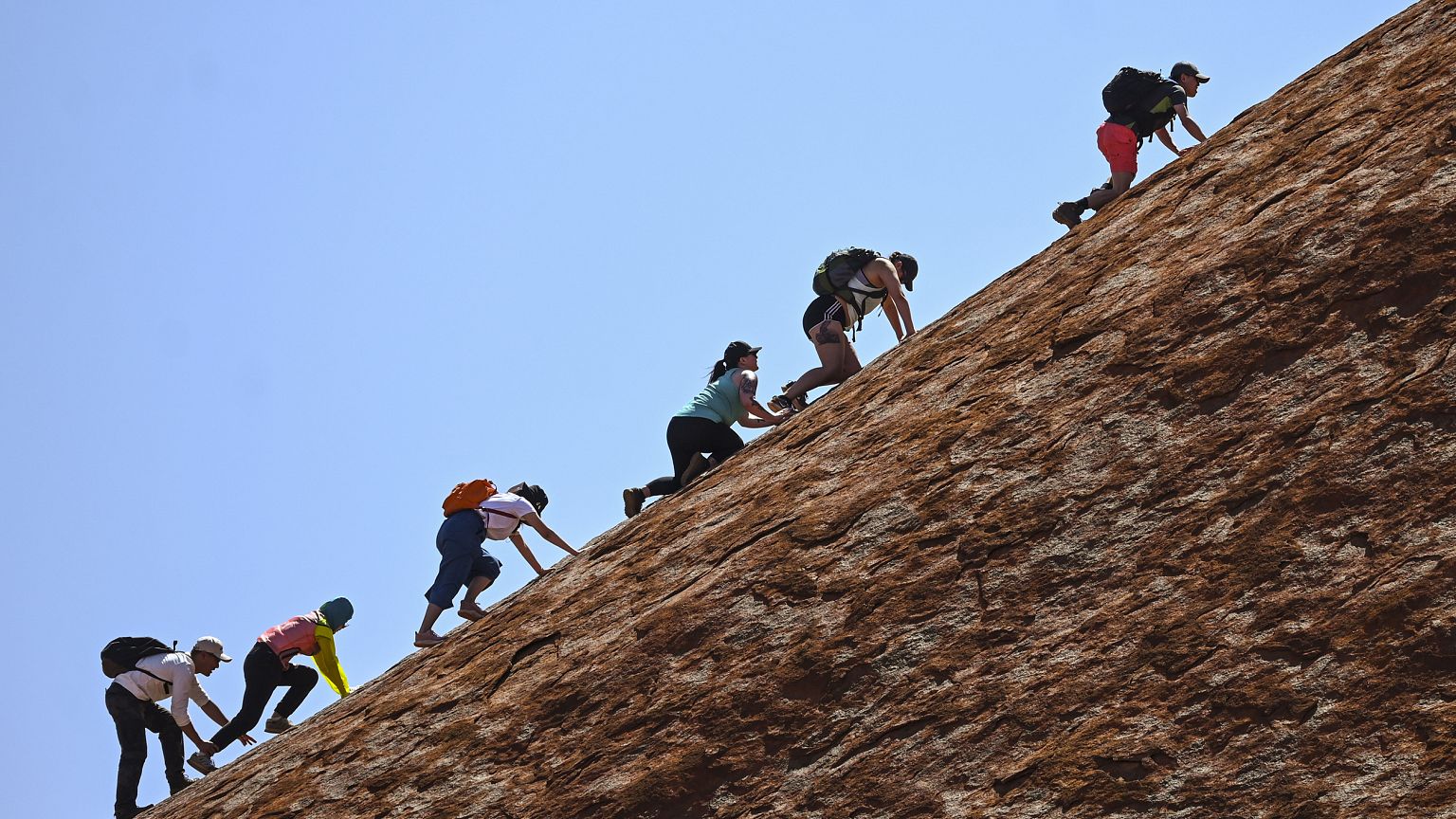 Image: Tourists climb Uluru.