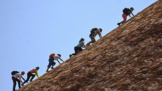 Image: Tourists climb Uluru.