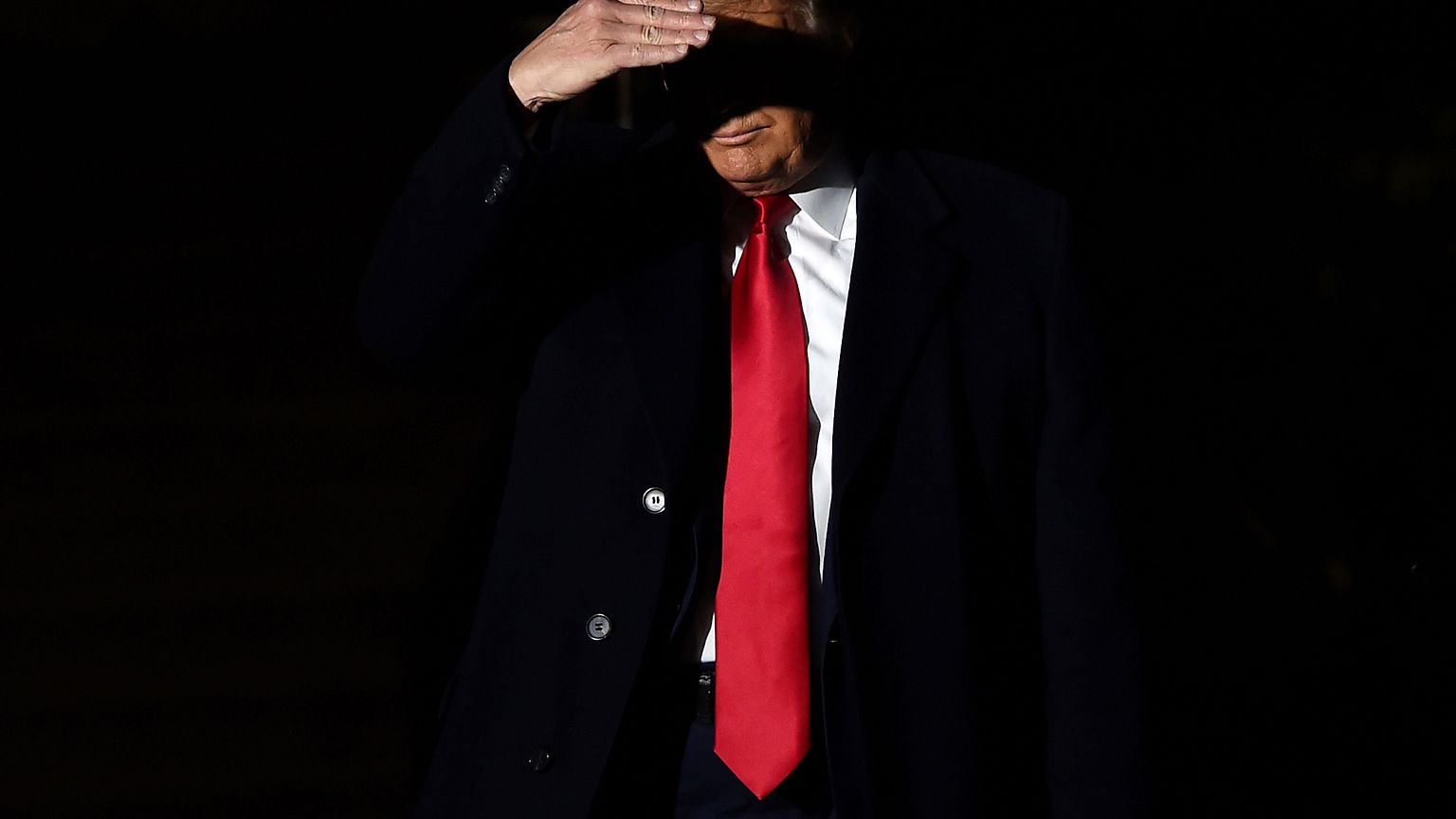 Image: President Donald Trump covers his face from TV lights as speaks to r